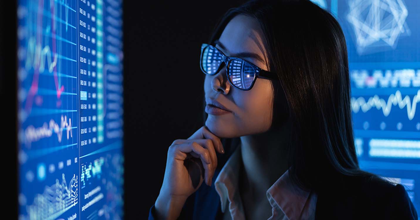 Woman wearing glasses analyzing data on a monitor
